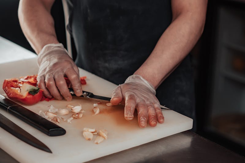 Crushing and chopping garlic cloves on white chopping board