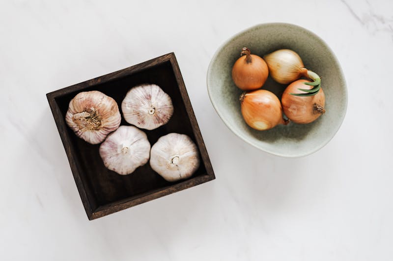 Garlic and onions in bowls on a marble countertop