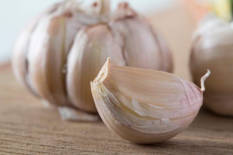 Close-up of a garlic clove with a whole garlic bulb in the background