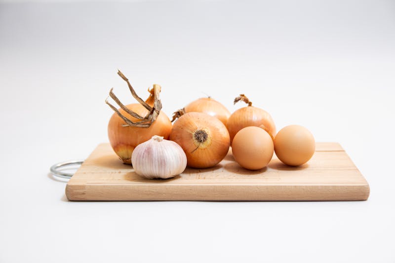 Onion and garlic on a wooden cutting board against a white background
