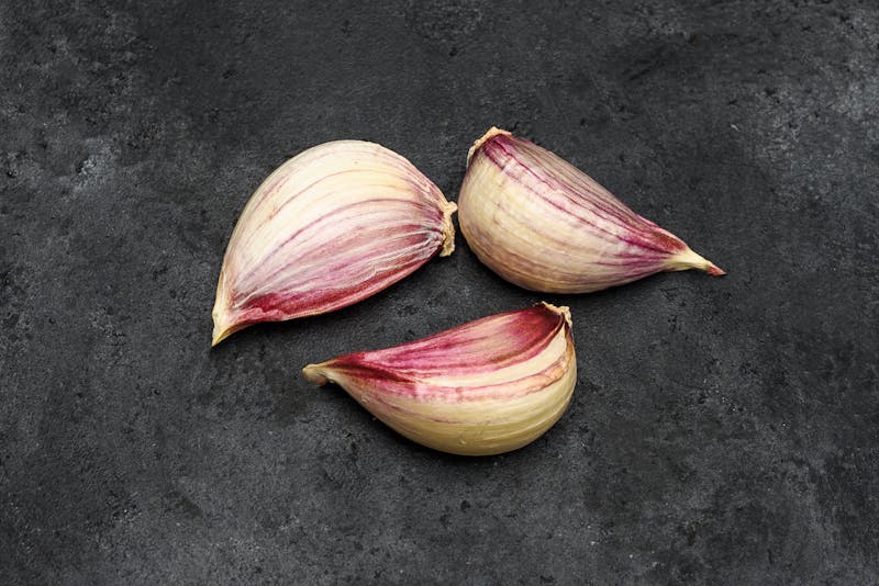 Three purple cloves of garlic on a dark background