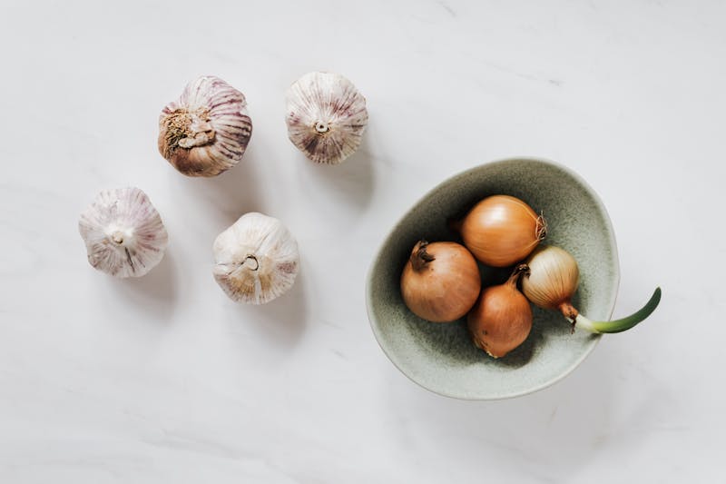 garlic bulbs and onions in a bowl, white background