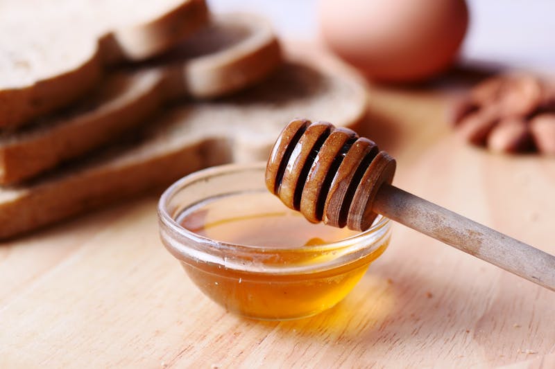 honey in a bowl with a honey dipper on wooden table